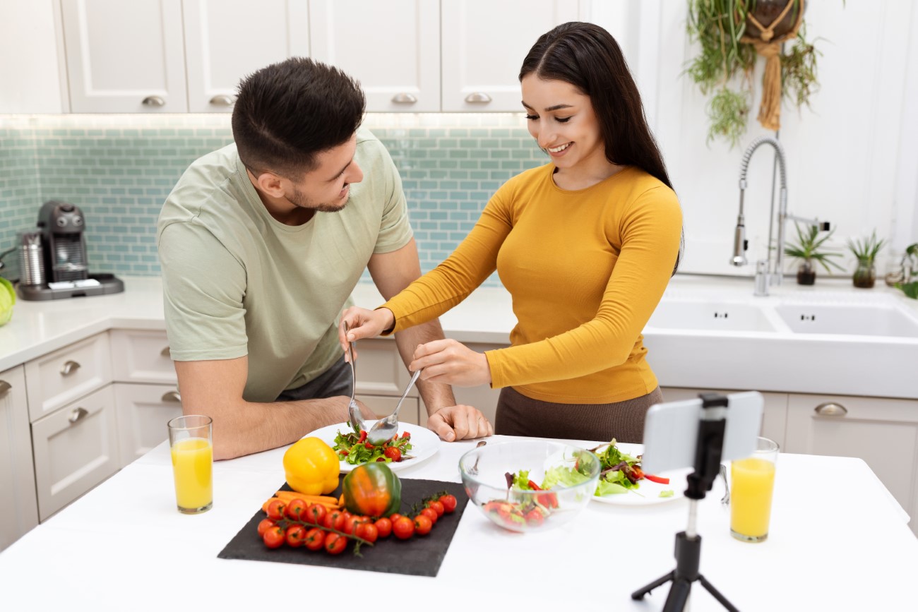 Beautiful loving spouses making food, watching video content on smartphone