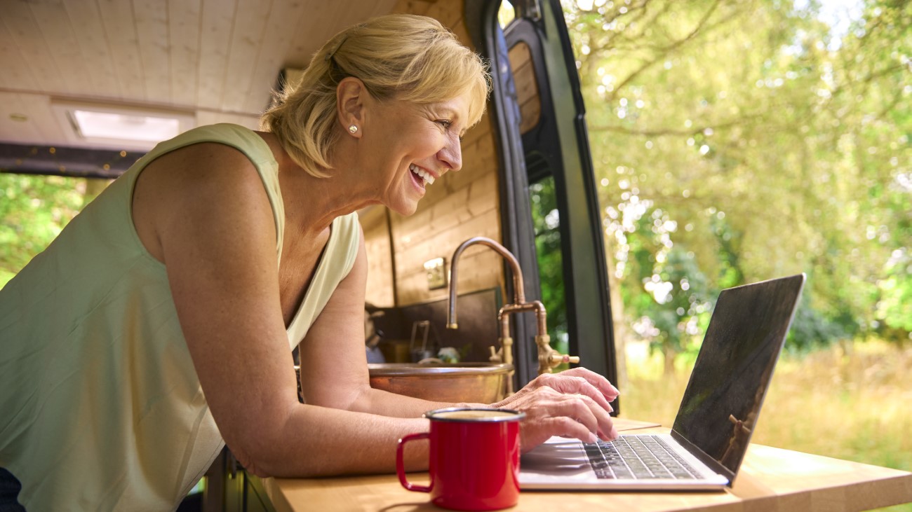 Senior Woman On Camping Trip In Countryside Working Inside RV Using Laptop