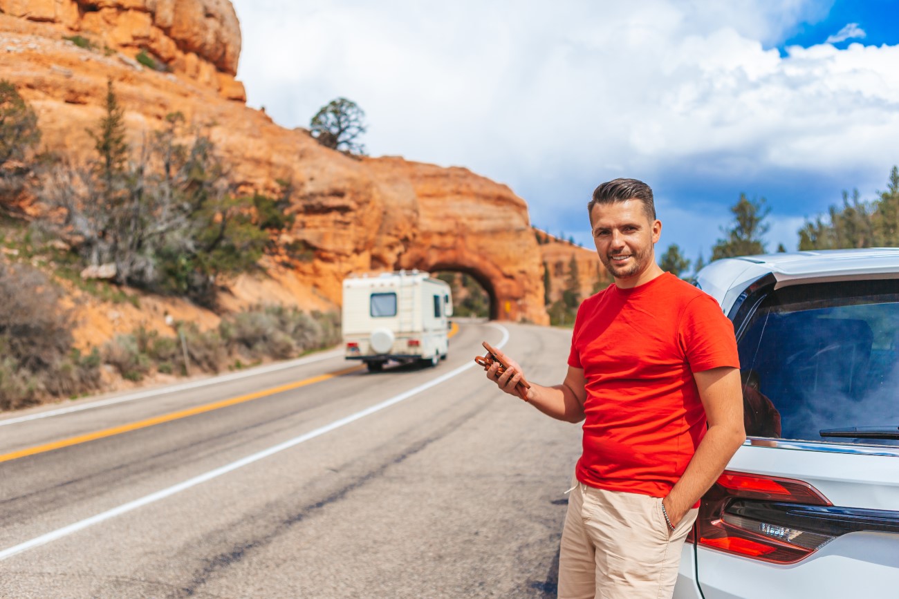 Young caucasian man in background of natural stone arch Bridge in the Red Canyon National Park in Utah, USA